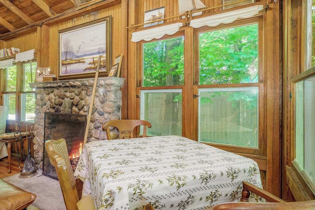 A cozy room with a stone fireplace, wooden walls, a bed with a floral bedspread, and large windows with a view of greenery.