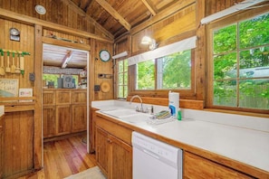 A wooden cabin interior with a kitchen area, wooden cabinets, a sink, and a dishwasher.