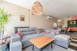A living room with a sectional sofa, a wooden coffee table, a large woven pendant light, and a potted plant.