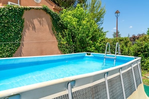 Piscina exterior con escalera, rodeada de vegetación y un farol.