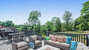 Eine Terrasse mit Korbmöbeln, einem Grill und Blick auf eine grüne Landschaft.