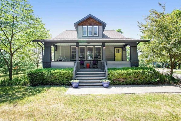 A two-story house with a front porch, a staircase leading to the entrance, and a well-maintained lawn.