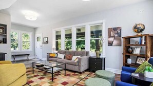 Ein Wohnzimmer mit einer Couch, Poufs, einem Couchtisch und einem Bücherregal.