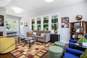 A living room with a sofa, ottomans, a coffee table, and a bookshelf.
