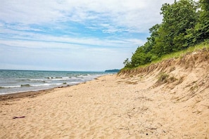 A sandy beach with gentle waves, a grassy cliff, and a clear sky. - Spacious Family Villa Near Beaches with Private Pool, WiFi, Firepit & Central AC (Union Pier)