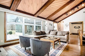 A spacious living room with a large window, a wooden ceiling, and a sofa with a coffee table. - Spacious Family Villa Near Beaches with Private Pool, WiFi, Firepit & Central AC (Union Pier)