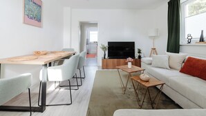 Uma sala moderna com sofá, televisão e área de jantar com cadeiras e mesa.
