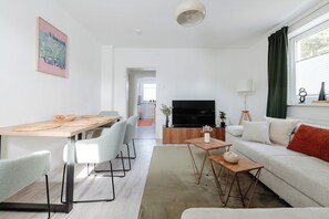 Ein modernes Wohnzimmer mit einer Couch, einem Fernseher und einem Essbereich mit Stühlen und einem Tisch.