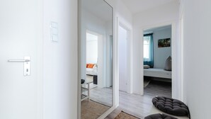Um interior moderno com uma porta branca, um espelho, um sofá, uma cama e um tapete pequeno.