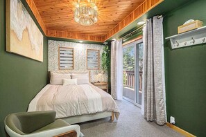 Ein Schlafzimmer mit Bett, Stuhl, einer Deckenleuchte, einem Fenster mit Vorhängen und Blick ins Freie.
