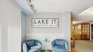 Et værelse med to blå lænestole, et lille rundt bord og et skilt på væggen med teksten 'LAKE IT or leave it'.