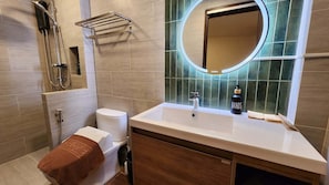 Un baño moderno con inodoro, lavamanos, ducha y espejo con marco circular.