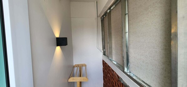 A narrow corridor with a wall-mounted light fixture, a wooden chair, and a window with a metal frame. - Old City Hall Contactless Check In (Bangkok)