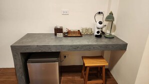 Uma cozinha compacta com geladeira embutida, um banquinho de madeira, cafeteira e uma luminária na bancada.
