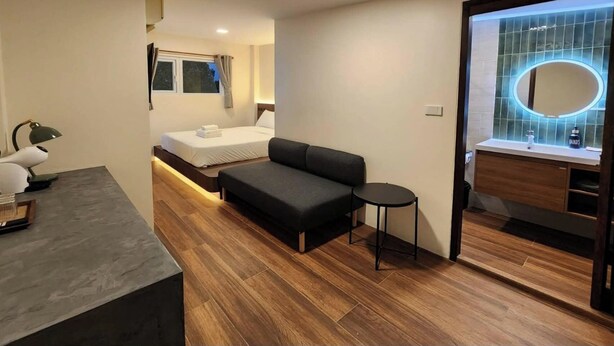 Quarto de hotel moderno com uma cama, um sofá, uma mesinha, um espelho e um banheiro com toucador.