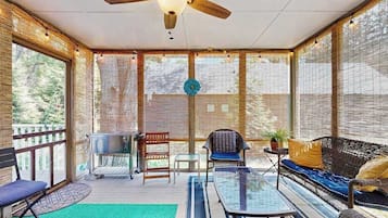 A covered outdoor area with a ceiling fan, a grill, seating, and large windows.