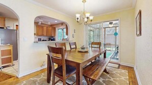 A dining area with a wooden table and chairs, a chandelier, and a view of the outside through glass doors. - Dog-Friendly Home with Enclosed Yard & Free High-Speed WiFi - Great Location (Union Pier)