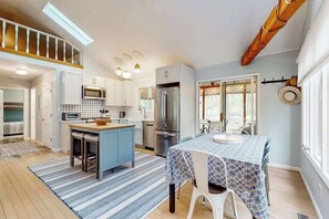 A modern kitchen with a central island, stainless steel appliances, and a dining area with a table and chairs. - Charming cottage with gas grill, golf cart, central AC, washer/dryer (New Buffalo)