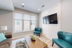 A living room with a sofa, a coffee table, and a TV mounted on the wall. - Cozy downtown TC ground floor condo, across from Grand Traverse Bay (Traverse City)