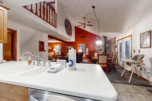 A kitchen with a large island, a dining area with chairs, a staircase, and a ceiling fan. - Spacious Home with deck, grill  & added Crystal Mountain Amenities (Thompsonville)