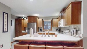 Eine Küche mit Holzausstattung, einem Edelstahlkühlschrank, einer Mikrowelle, einem Spülbecken und einer Bar mit Hockern.
