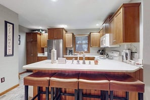A kitchen with wooden cabinets, a stainless steel refrigerator, a microwave, a sink, and a bar area with stools. - Spacious Home with deck, grill  & added Crystal Mountain Amenities (Thompsonville)