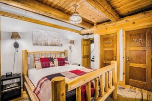 A wooden-framed bed with a quilt, two bedside lamps, and a wall-mounted abstract painting.