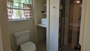 Ein Badezimmer mit Toilette, einer Dusche mit Glastür, einem Fenster mit Vorhängen und einem gefliesten Boden.
