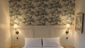 Ein Bett mit zwei Kissen, zwei Nachttischen, einem Deckenventilator und einer Wand mit floralem Tapetenmuster.