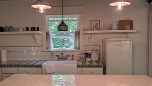 Eine Küche mit einer großen Kochinsel, hängenden Pendelleuchten, einem Fenster mit Vorhängen und einem Kühlschrank.
