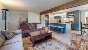 A modern living room with a sofa, coffee table, and a kitchen area with bar stools. - Peaceful Home with Firepit, Gas Grill, WIFI,  Private W&D & Nearby Beach Access (St. Joseph)