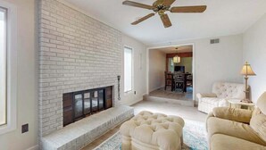 A living room with a fireplace, a ceiling fan, and a dining area in the background. - Peaceful Home with Firepit, Gas Grill, WIFI,  Private W&D & Nearby Beach Access (St. Joseph)