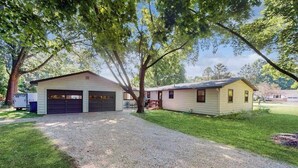 A two-story house with a garage, a covered porch, and a well-maintained lawn. - Peaceful Home with Firepit, Gas Grill, WIFI,  Private W&D & Nearby Beach Access (St. Joseph)