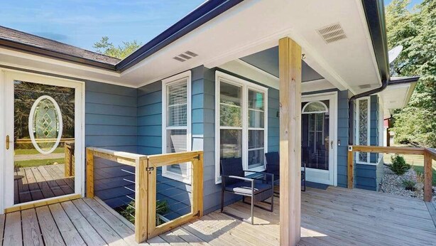 A covered deck with a wooden railing, a glass door leading to a patio, and a seating area with a table and chairs. - Lovely home with hot tub, pool, two kitchens, enclosed backyard, firepit & grill (New Buffalo)
