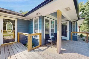 Une terrasse couverte avec une rambarde en bois, une porte vitrée donnant sur un patio et un espace salon avec une table et des chaises.
