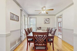A dining area with a wooden table and chairs, a ceiling fan, and a framed quote on the wall. - Lovely home with hot tub, pool, two kitchens, enclosed backyard, firepit & grill (New Buffalo)