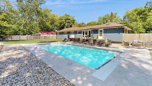 A backyard with a swimming pool, a covered patio, and a wooden fence. - Lovely home with hot tub, pool, two kitchens, enclosed backyard, firepit & grill (New Buffalo)