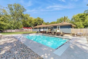 A backyard with a swimming pool, a covered patio, and a wooden fence. - Lovely home with hot tub, pool, two kitchens, enclosed backyard, firepit & grill (New Buffalo)