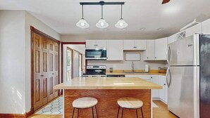 A modern kitchen with a central island, bar stools, a stainless steel refrigerator, and wooden cabinets. - Lovely home with hot tub, pool, two kitchens, enclosed backyard, firepit & grill (New Buffalo)