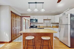 A modern kitchen with a central island, bar stools, a stainless steel refrigerator, and wooden cabinets. - Lovely home with hot tub, pool, two kitchens, enclosed backyard, firepit & grill (New Buffalo)