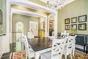 A dining area with a dark wooden table, white chairs, and a chandelier. - Luxurious home with woodstove, fireplace, & screened porch - walk everywhere (Saugatuck)