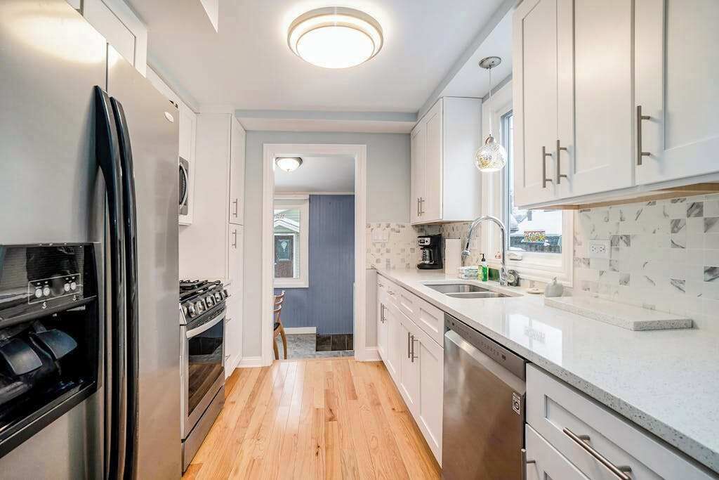 Et moderne køkken med rustfrie hårde hvide skabe og trægulv.