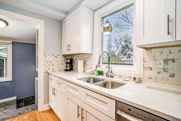 Una cocina moderna con armarios blancos, un lavamanos doble y una ventana con vistas a árboles.