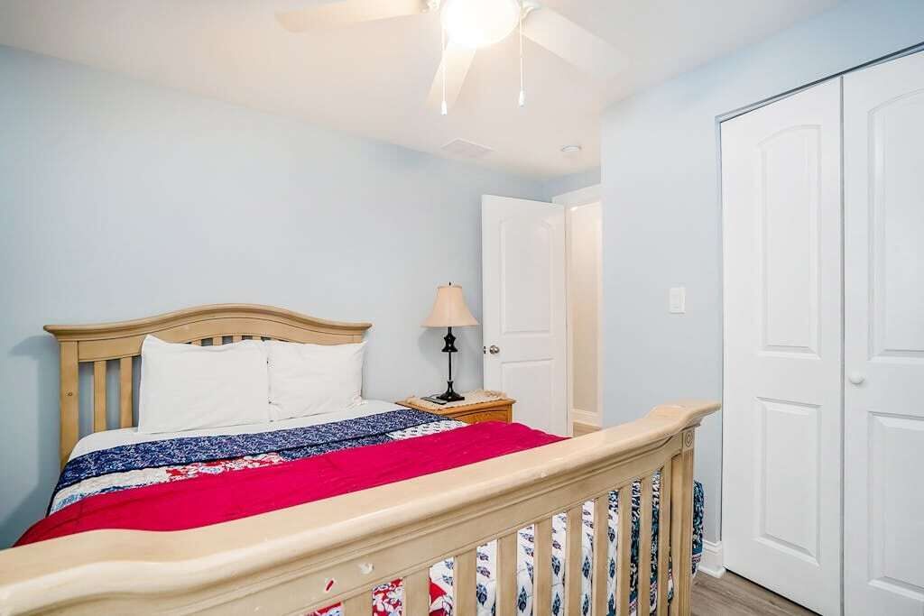 A bedroom with a bed, a nightstand, a lamp, a ceiling fan, and a door.