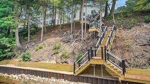 Eine Holztreppe führt einen Hügel hinauf, mit Blick auf ein modernes Haus im Hintergrund.