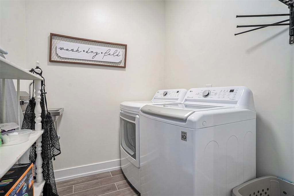 Een wasserette met een voorlader wasmachine en droger, een plank met wasmiddelen, en een bordje in een lijst aan de muur.