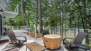 Eine Terrasse im Freien mit Korbmöbeln, einem runden Tisch mit einer beige-farbenen Tischdecke und Blick auf ein bewaldetes Gebiet.