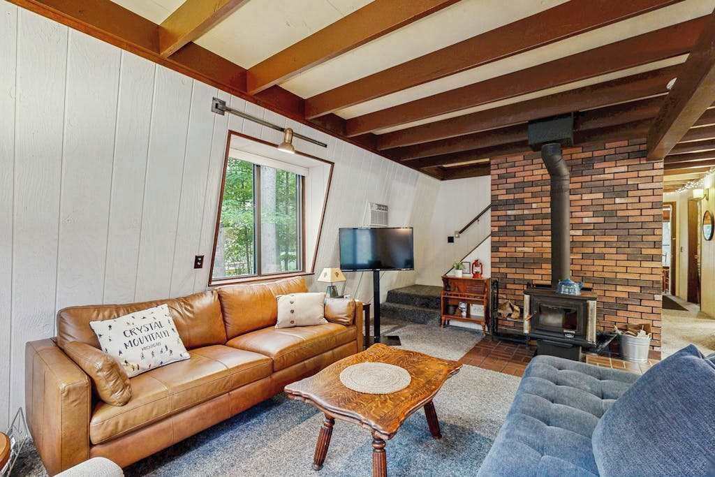 Un salon avec un canapé en cuir, une table basse en bois, un téléviseur et une cheminée en briques.