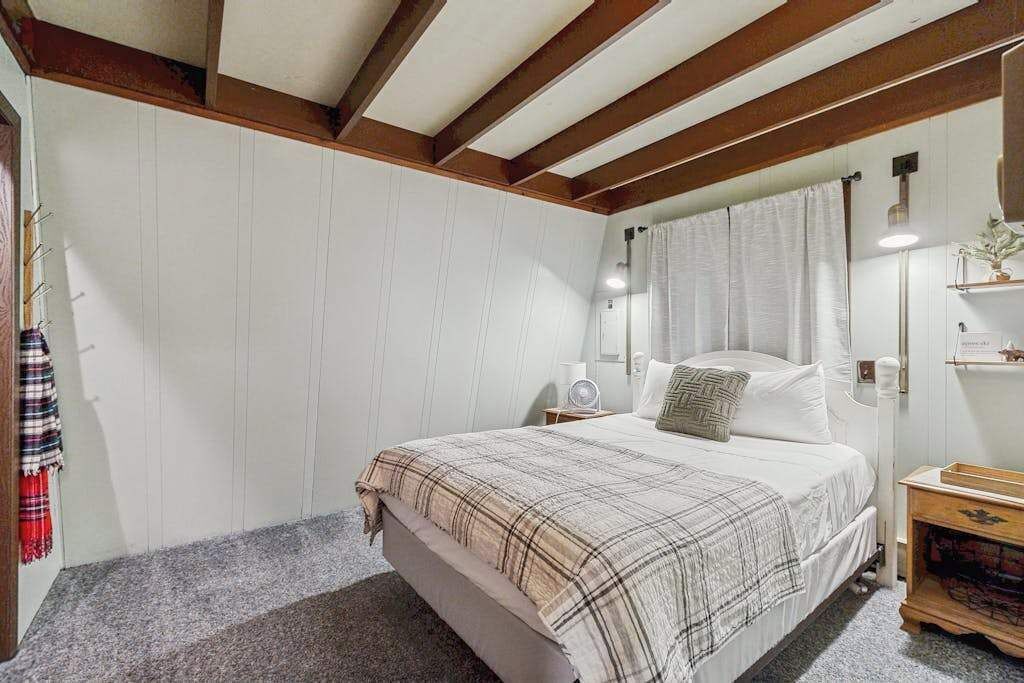 Een slaapkamer met een bed, nachtkastje, spiegel en raam met gordijnen.