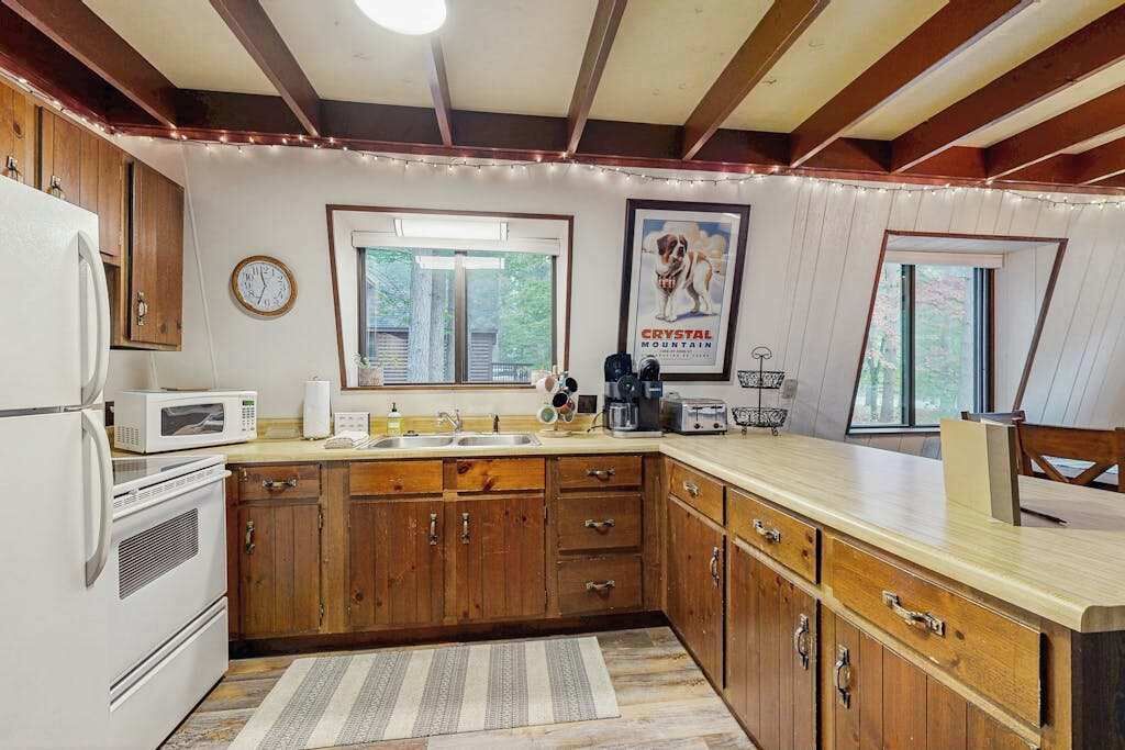 Una cocina con armarios de madera, un refrigerador blanco, un microondas, un lavamanos y una ventana con vista a árboles.
